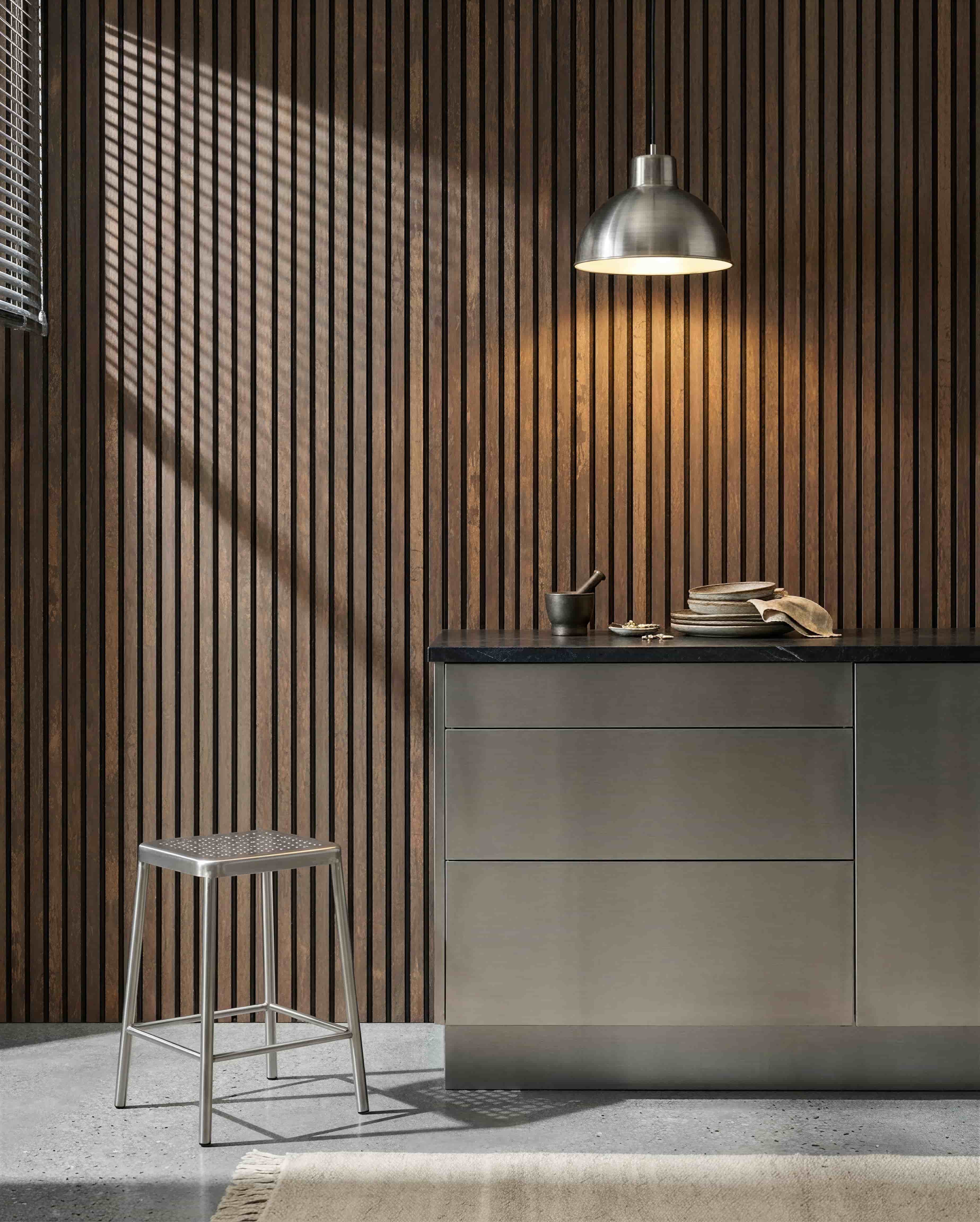 Kitchen featuring a WoodUpp Akupanel Oxide Copper acoustic slatted wall, stainless countertop, metal stool, pendant light, assorted dishes, and mortar  pestle.
