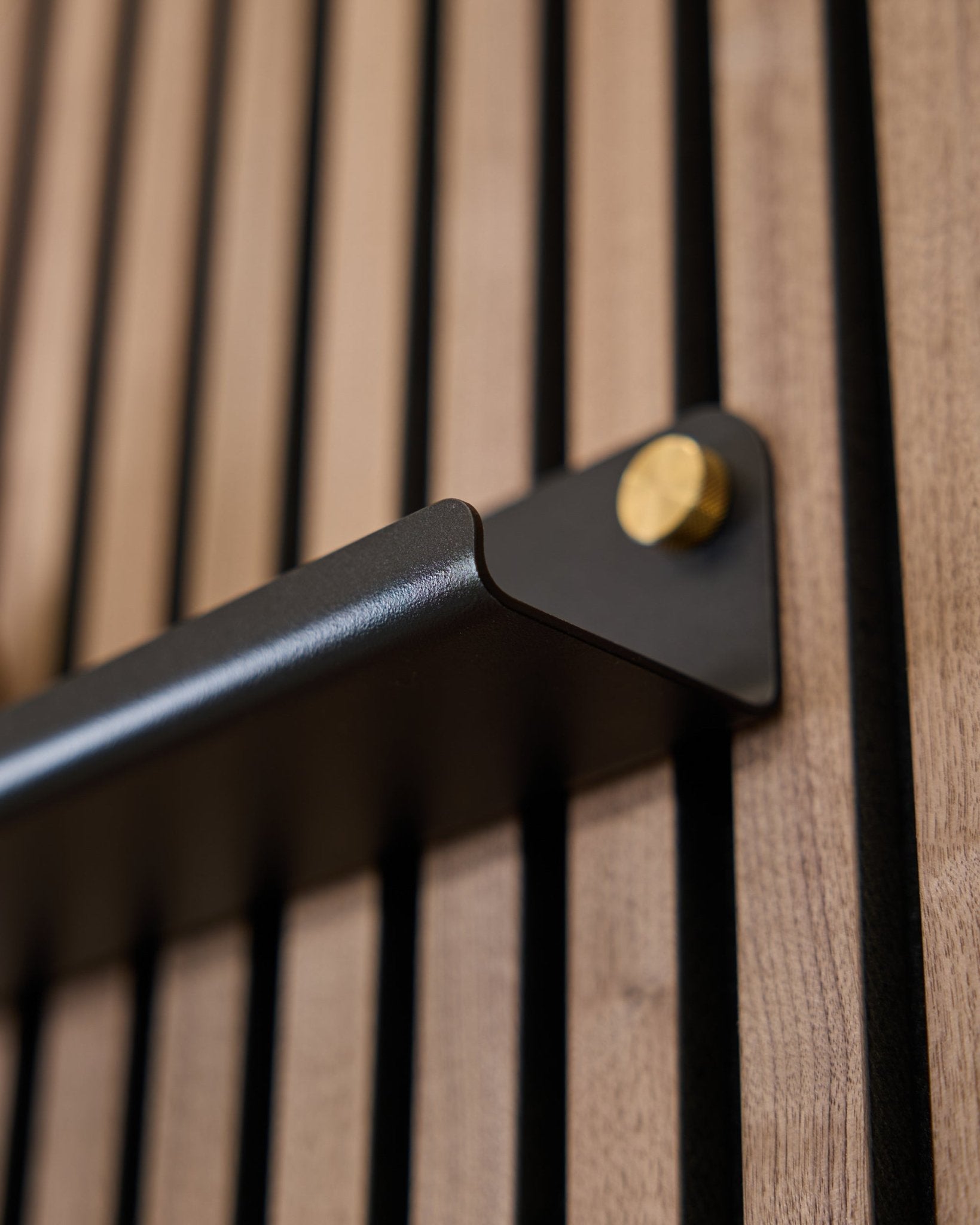 Close-up of the Norr | Narrow Shelf (75.9 cm) by WoodUpp in black, featuring a steel handle with gold bolts and vertically grooved acoustic surface.