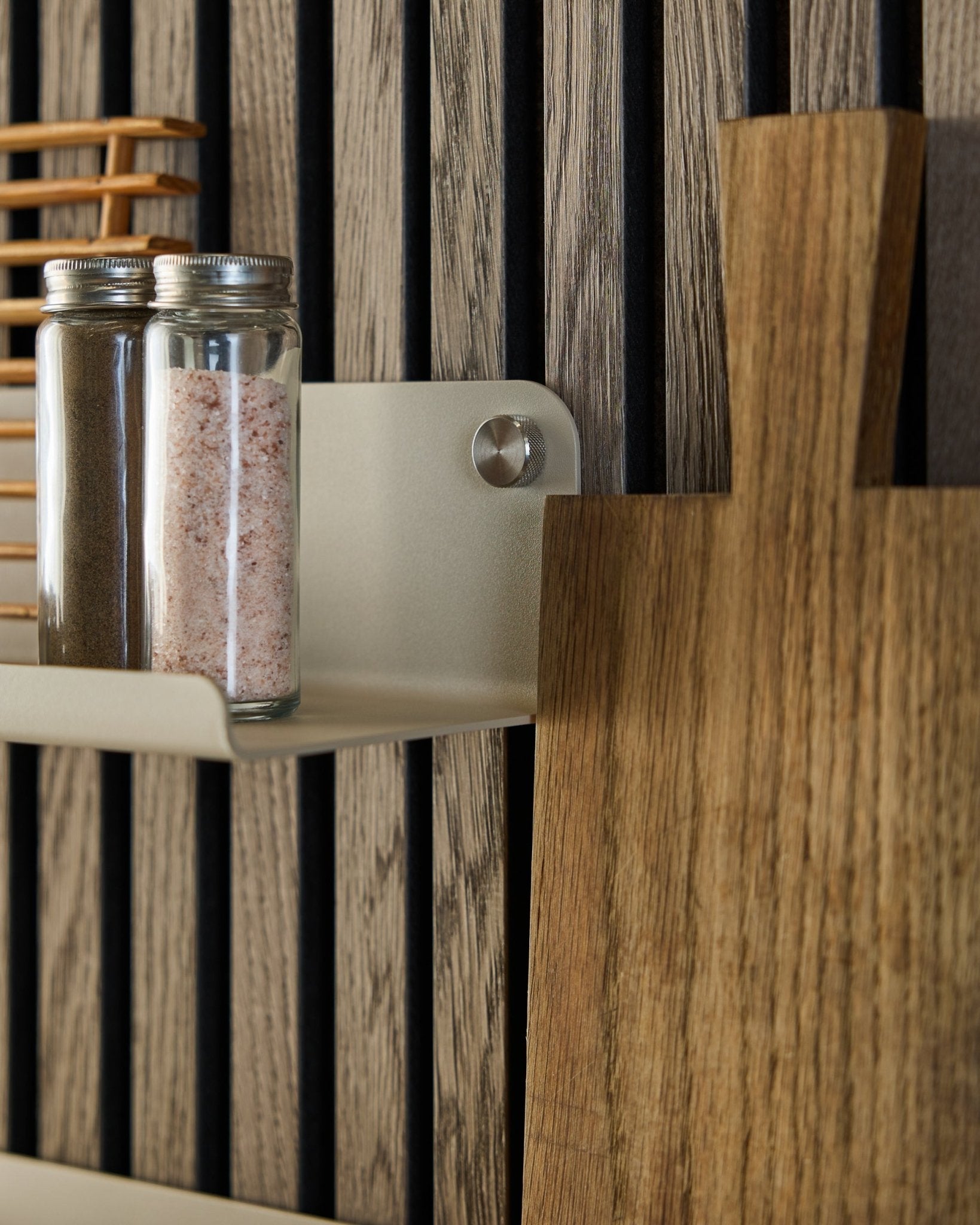 Glass jars with spices and a wooden cutting board rest on the WoodUpp Norr Wide Shelf in beige, 35.9 cm, mounted against a vertical acoustic slatwall panel.