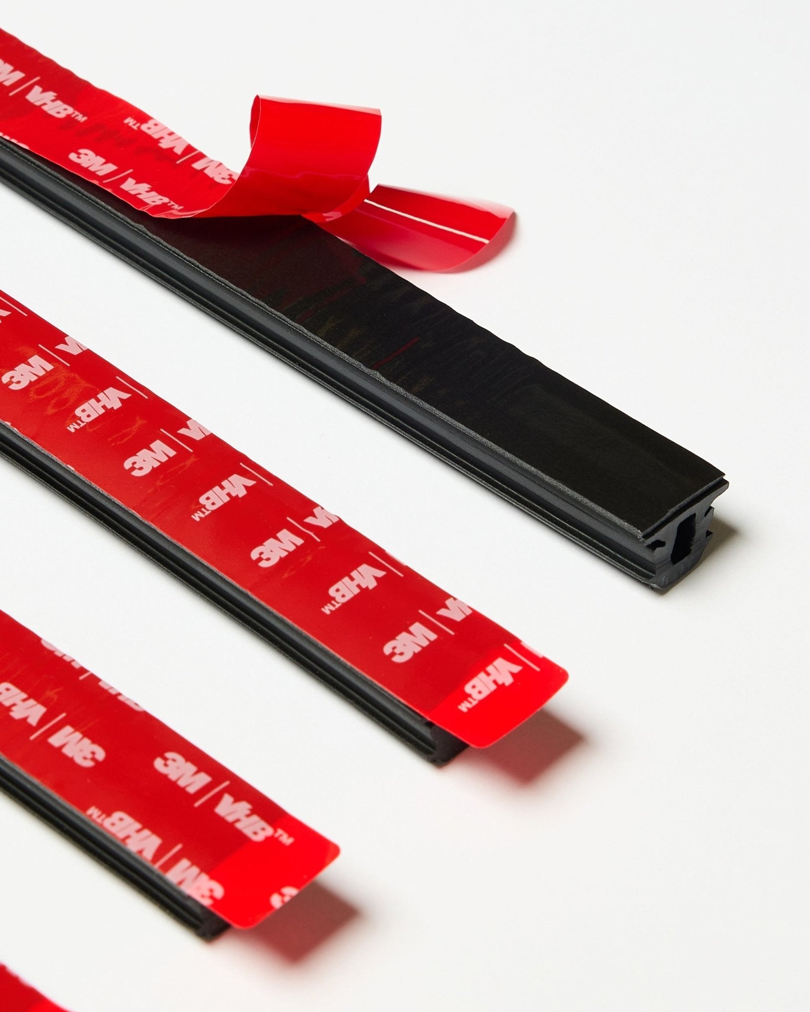 Set of four black WoodUpp CREATE Pop-on Profile strips with visible red 3M adhesive backing, one strip partially peeled, displayed on a white surface.
