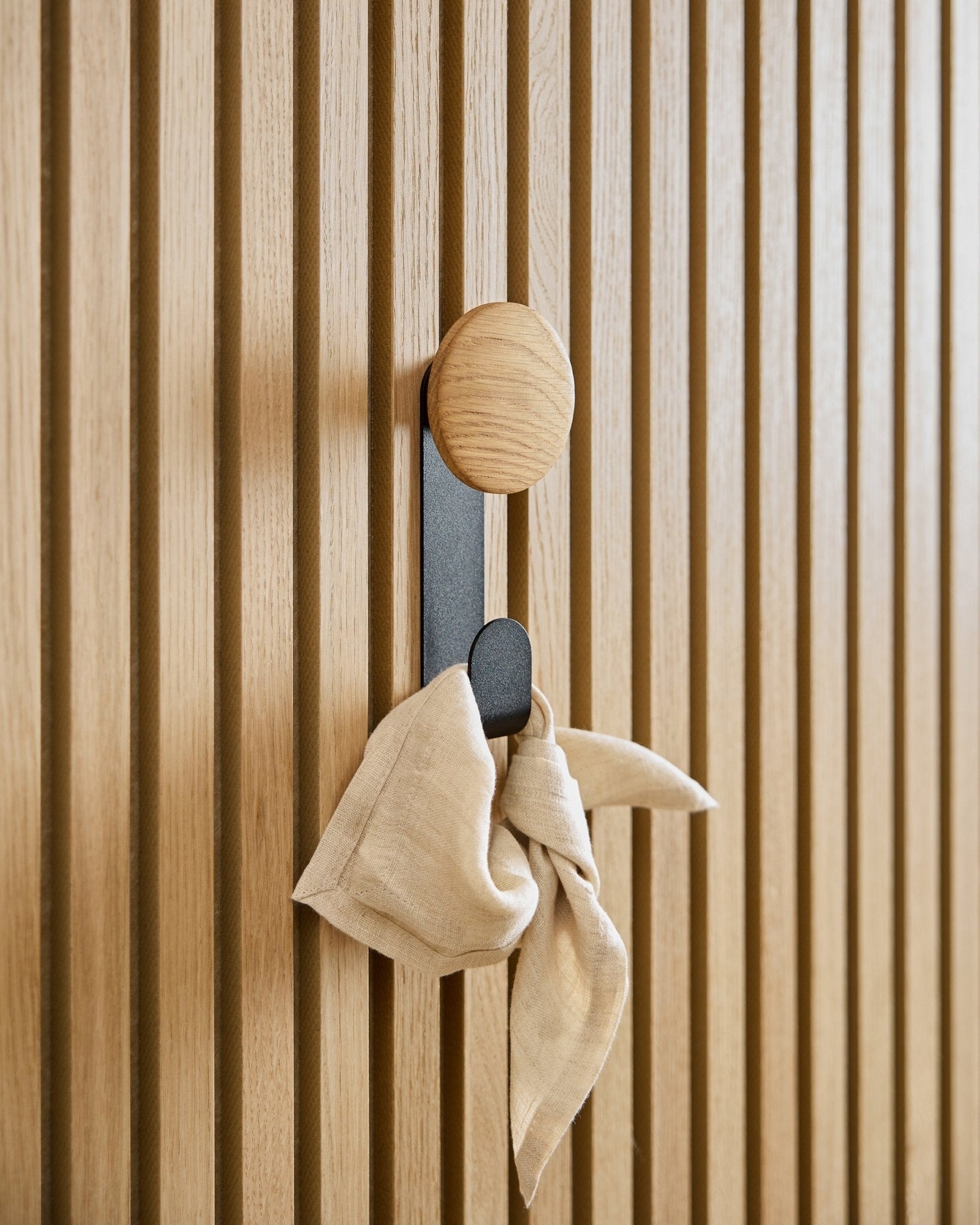 A beige cloth hangs from the Linn Vertical Hanger in Natural Oak by WoodUpp, mounted on a vertical Akupanel acoustic slatwall panel.