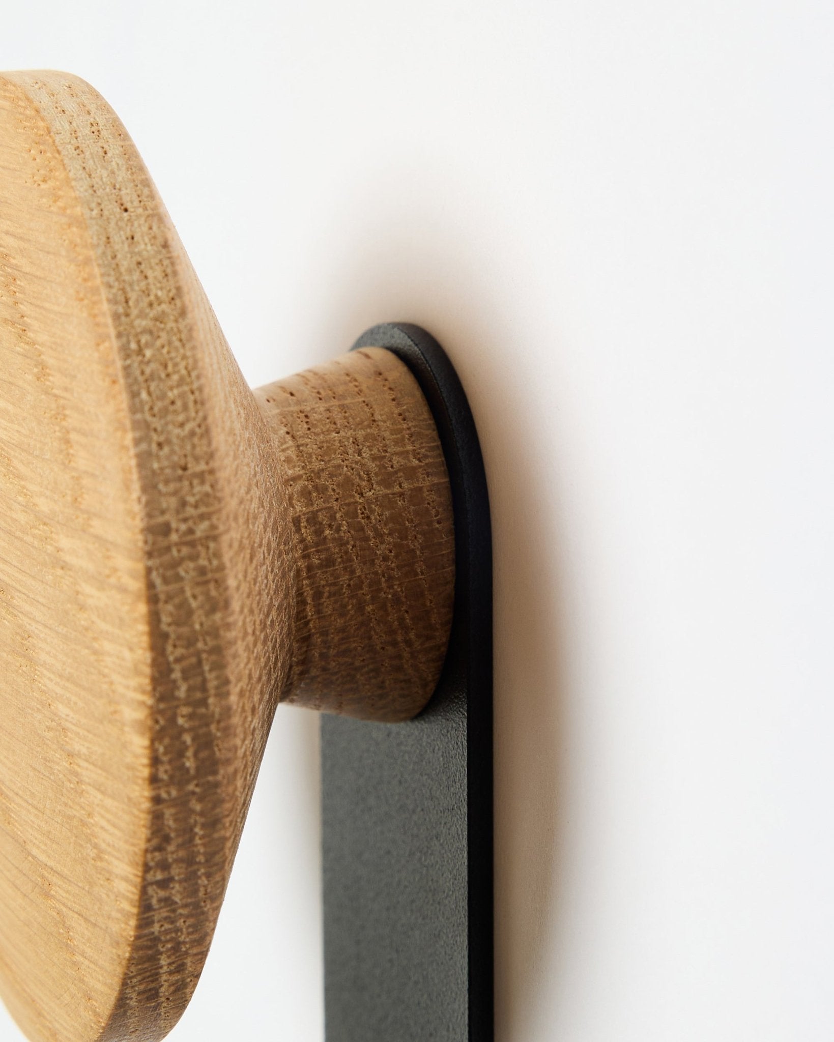 Close-up of the Linn Vertical Hanger in natural oak by WoodUpp, a round wood knob accessory mounted on a black bracket, designed for Akupanel acoustic panels.