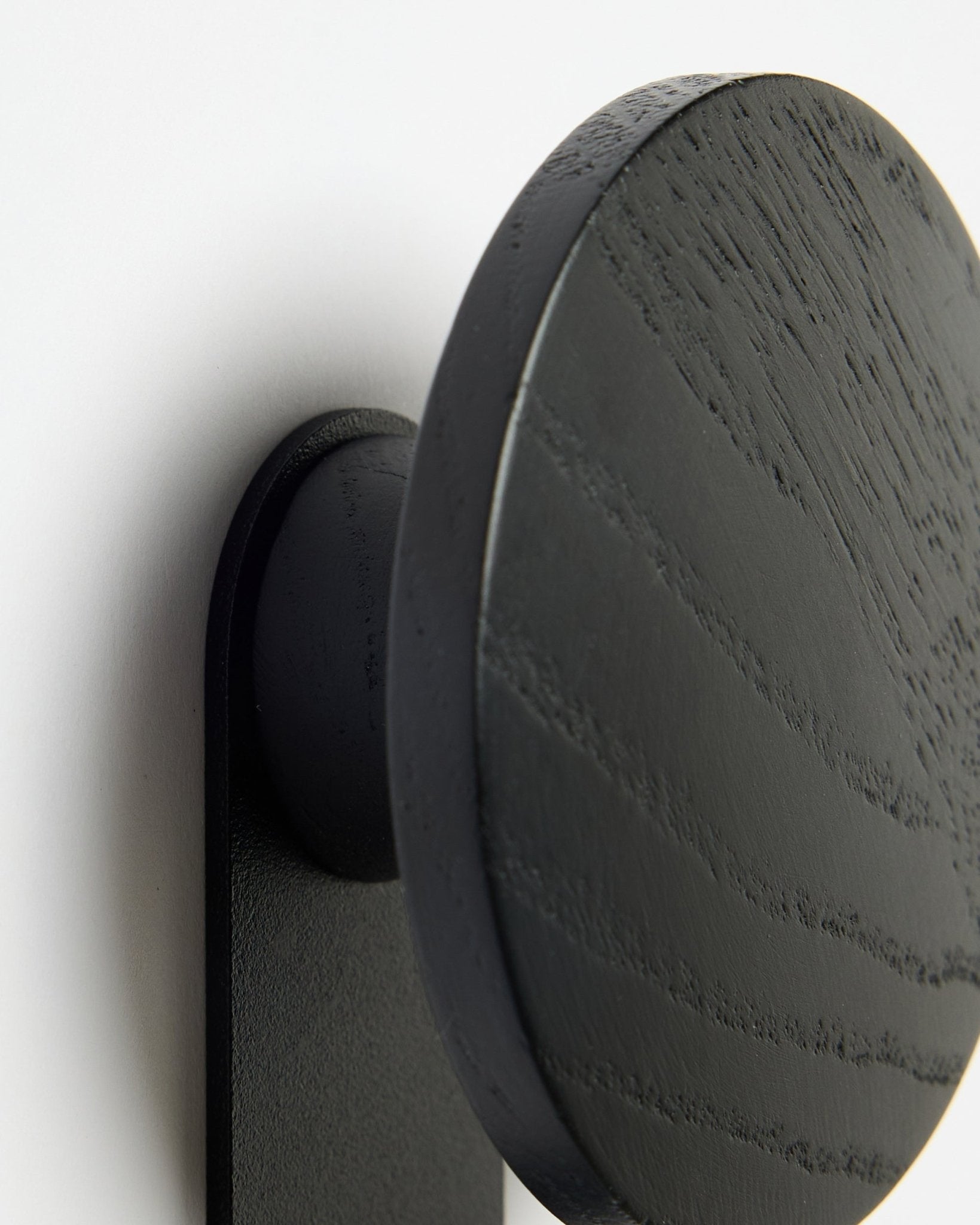 Close-up of WoodUpp Linn | Vertical Hanger in Black Oak, highlighting detailed wood grain against a white Akupanel acoustic panel background.