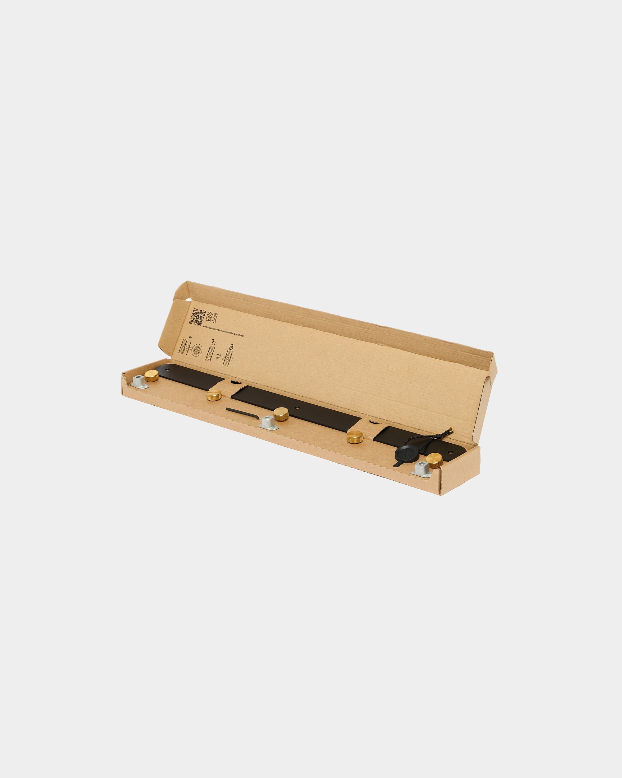 A long, rectangular cardboard box open to show neatly organized metal mounting components for Akupanel acoustic panels, displayed on a plain white background.