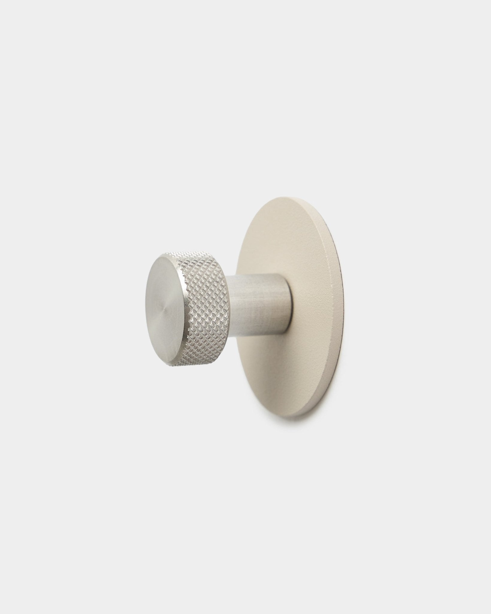 WoodUpp Norr Coat Hook in beige and stainless steel with a textured cylindrical end and round base, accessory for Akupanel, on a plain white background.