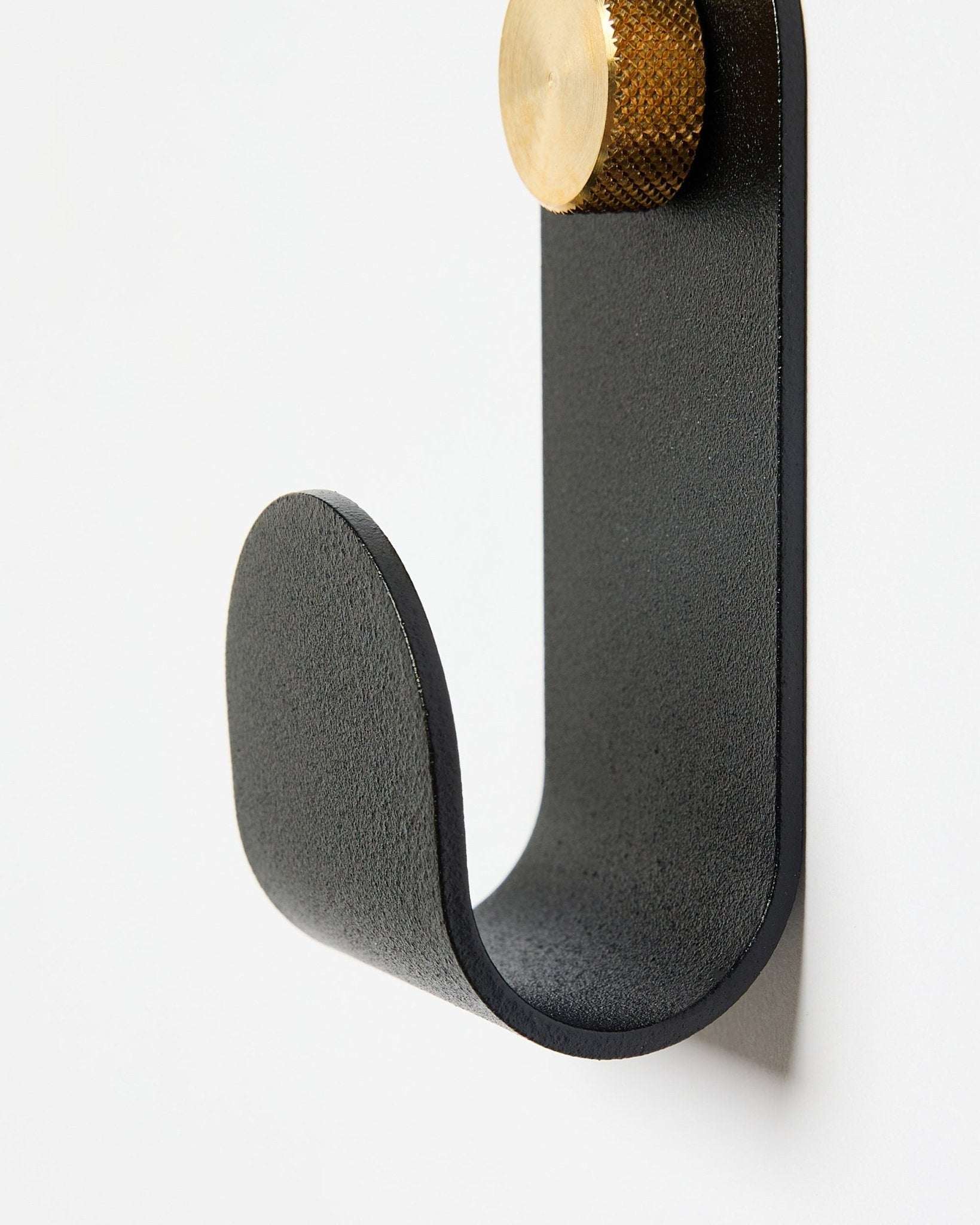 The Norr Single Hanger by WoodUpp has a black metal curved arm with a gold cap, designed as an accessory for use with acoustic panels on white walls.