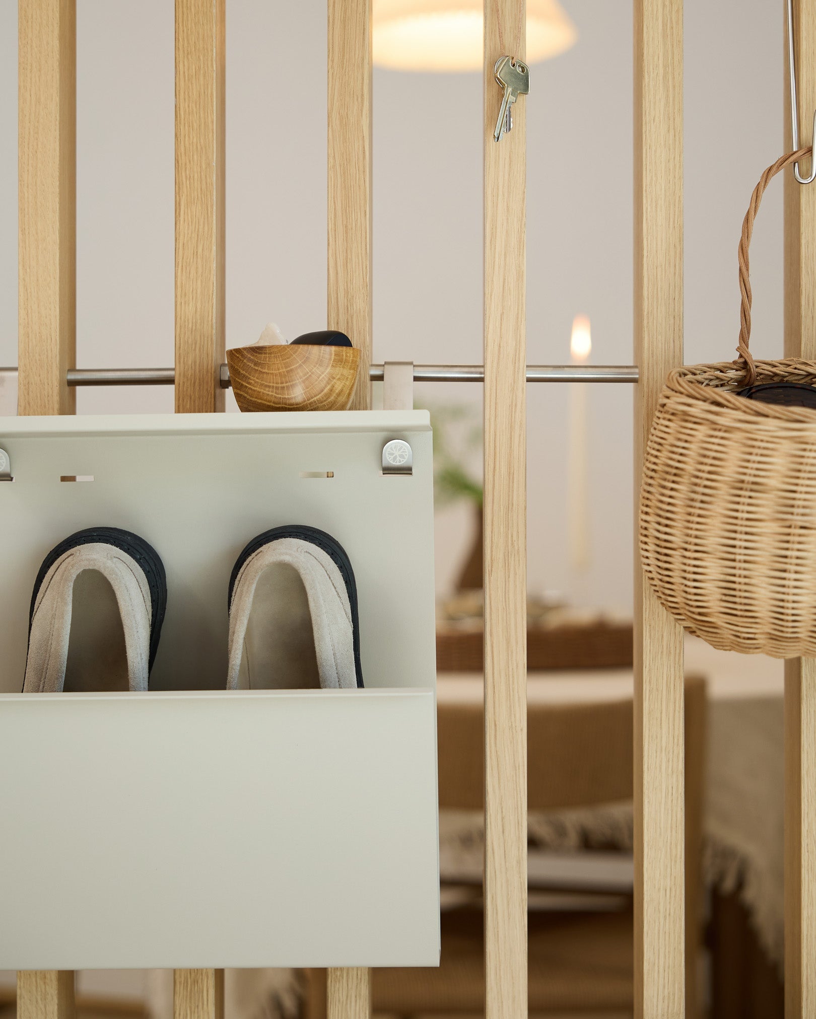 WoodUpp Nell Beige Shoe Storage displays slippers, a bowl, and a wicker basket on a wood room divider; dining area visible in the background.