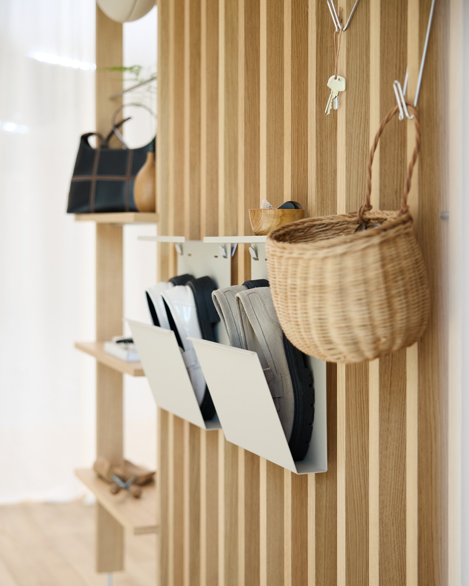Modern hallway with WoodUpp’s beige Nell Shoe Storage, Akupanel acoustic wood panel walls, wall hooks, a hanging basket, and a shelf displaying decor items.