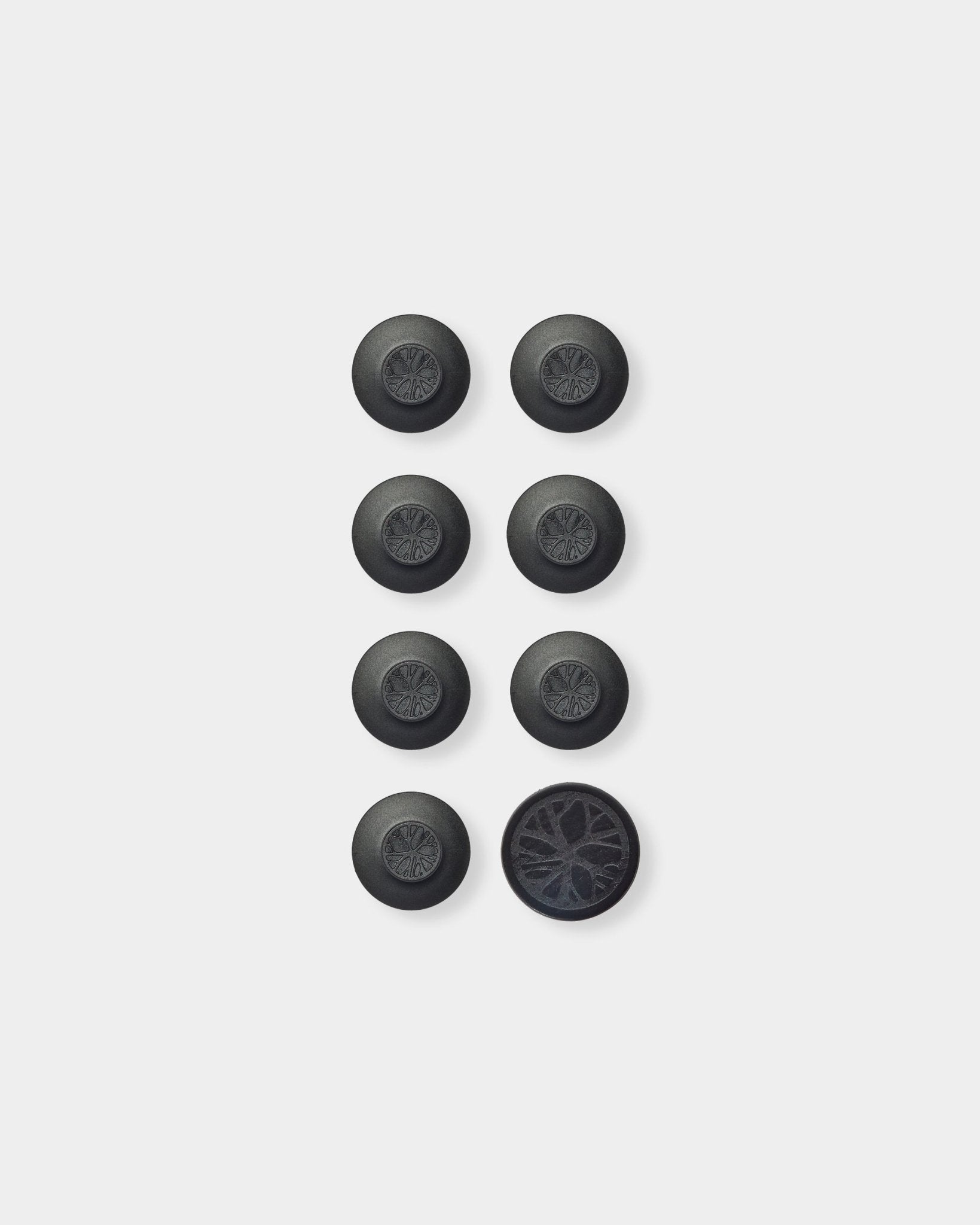 Seven round black Dupps acoustic panel accessories by WoodUpp and one tool arranged in a grid; bottom right Dupp flipped to show its textured underside.