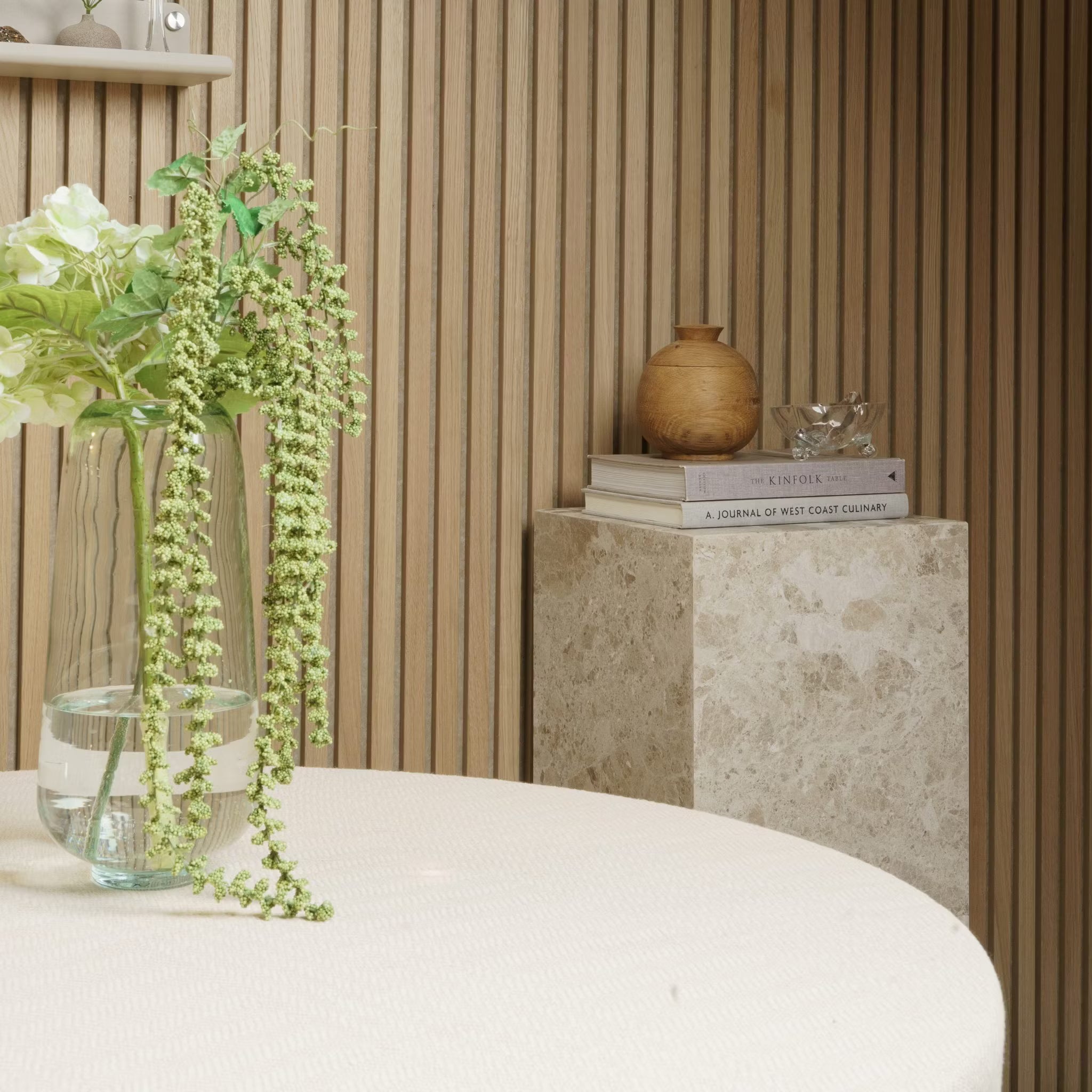 A vase with flowers sits on a round table; books and pottery rest on a marble pedestal against an Akupanel acoustic wood panel wall.