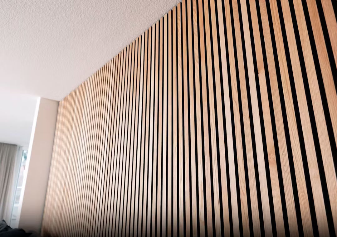 Close-up of Akupanel acoustic wood panel featuring vertical wooden slats in a striped pattern, installed on an interior wall beneath a white ceiling.