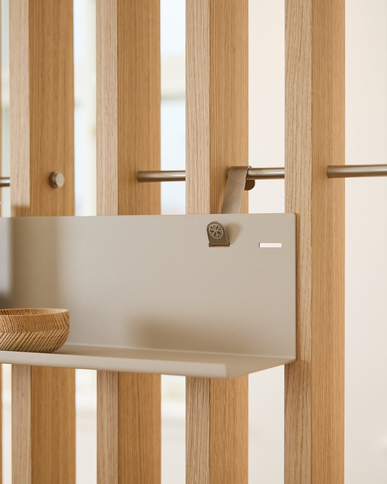 Beige WoodUpp BM1 metal shelf (63x13.4 cm) mounted on vertical acoustic slatwall panel, featuring a wooden bowl on the left side of the shelf.