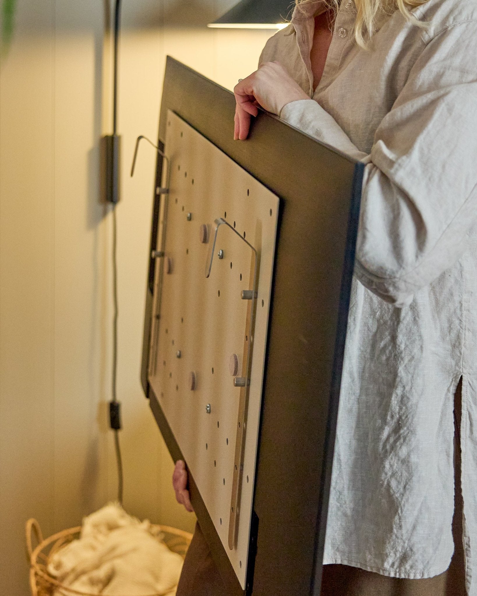 Individual in a light shirt holds the WoodUpp Nell BM1 TV-Mount in beige, 64x44cm—compatible with Nordic acoustic wood panels, for non-wall installations.