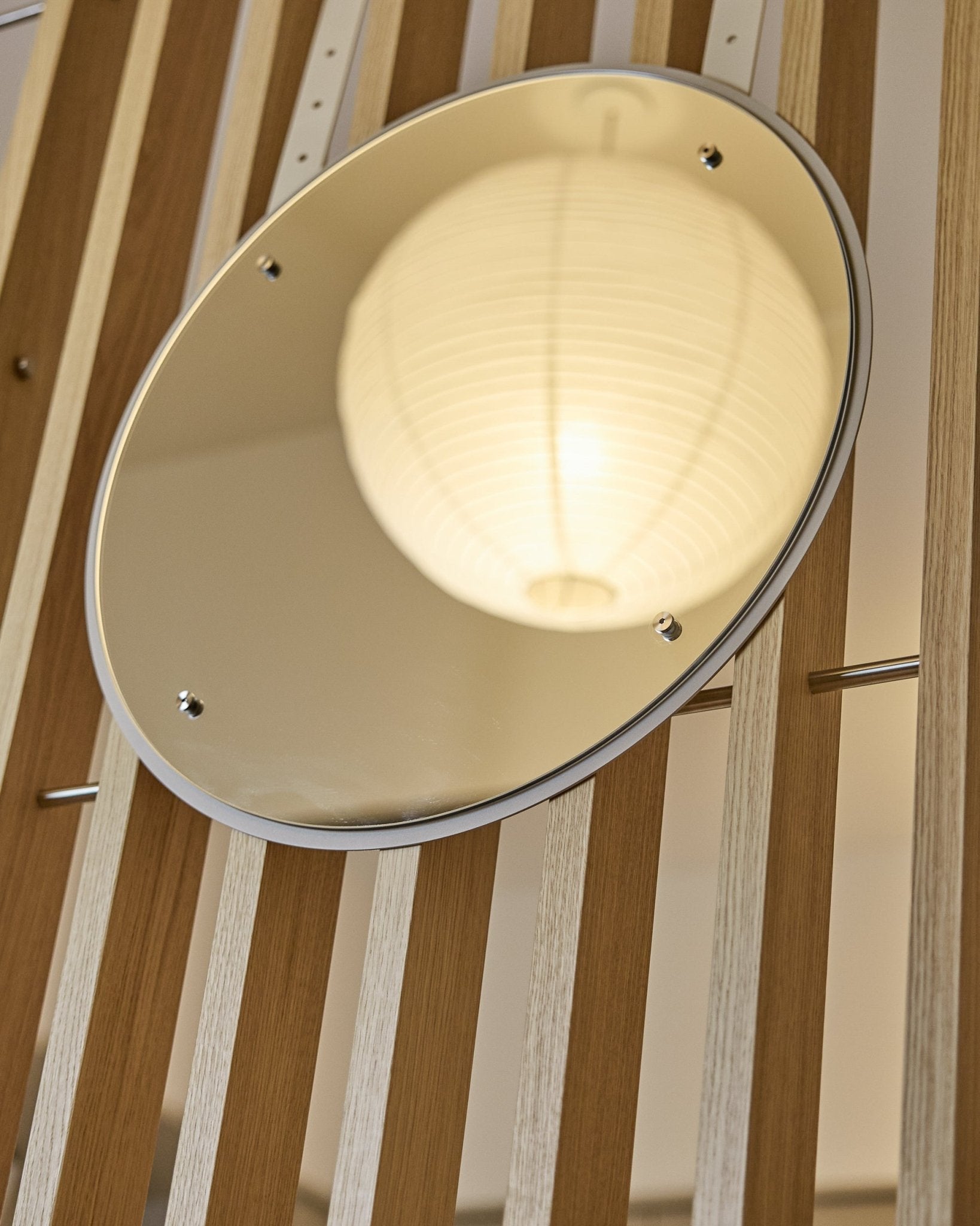 The Vala | Mirror / BM1, D54 cm by WoodUpp is a height-adjustable round mirror mounted on vertical acoustic slatwall panels, reflecting a glowing paper lantern.