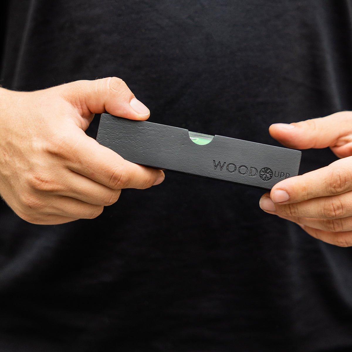 Person in a black shirt holds a black WoodUpp Spirit Level (15 x 3.2 cm), designed for precise installation of acoustic panels.